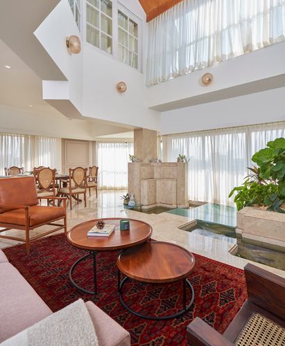 Double-height living room with marble floor, sunken water feature, and nesting wood coffee tables on a red rug