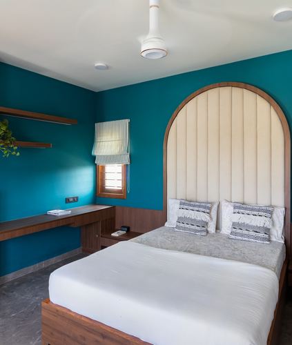 Teal bedroom with arched cream headboard, wooden bed, and built-in study desk