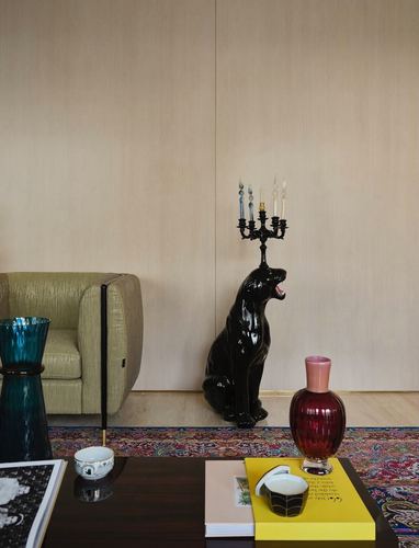 black ceramic dog sculpture holding a candelabra beside an olive armchair and patterned rug