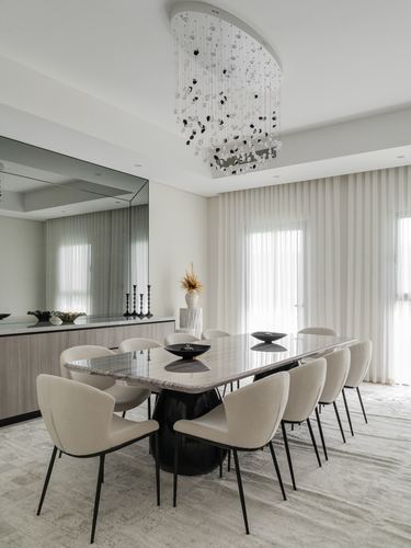 Dining room with long stone-top table, cream chairs, mirrored wall and sculptural chandelier