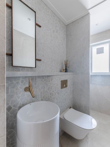 Grey stone-clad bathroom with pedestal basin, wall-hung toilet, and wood-framed mirror