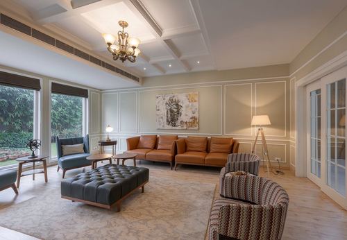 Living room with tan leather sofas, tufted ottoman, coffered ceiling and garden view windows