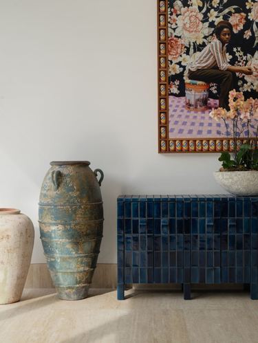 Weathered ceramic vases beside a blue tiled cabinet with framed art above
