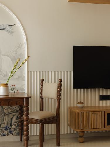 Living room corner with wooden spool chair, console table, arched crane mural panel, and wall-mounted tv over fluted paneling