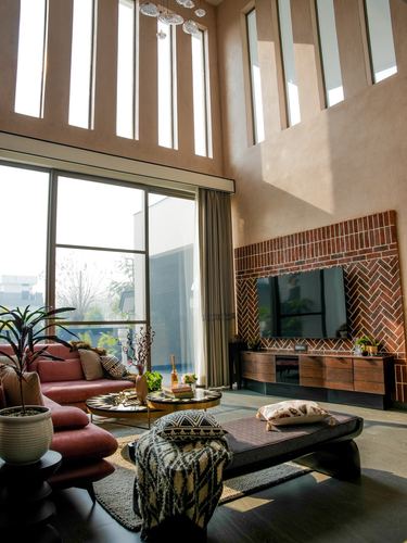 Double-height living room with herringbone brick TV wall, terracotta sofa, and tall slot windows