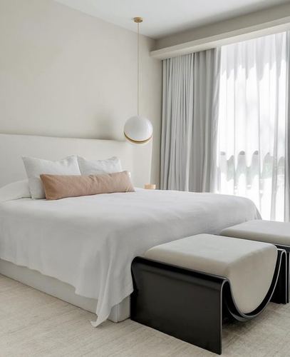 Minimalist neutral bedroom with white bed, pink lumbar pillow, globe pendant, and black curved benches