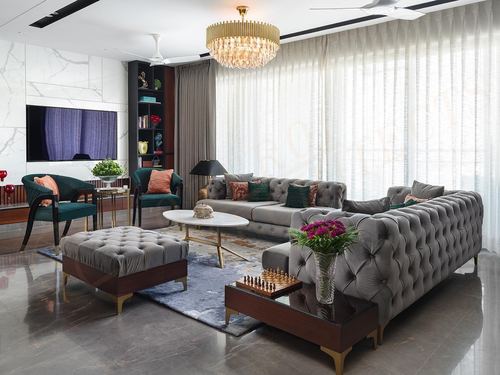 Luxurious living room with tufted grey sofas, teal armchairs, and a gold chandelier