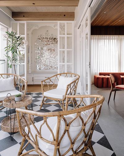 Living room with rattan chairs, checkerboard marble floor, and a carved jali panel with om motif