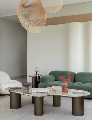 Living room with fan-shaped wood pendant, green velvet sofa, and organic stone coffee table on bronze cylindrical legs