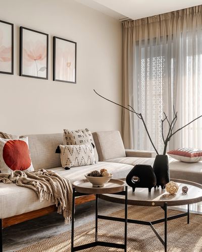 Beige sectional sofa with cushions beside round coffee tables and sheer curtained window in earthy living room