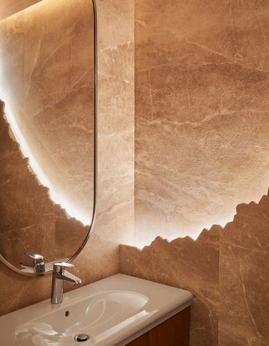 Backlit irregular mirror over stone-clad powder room sink with chrome faucet