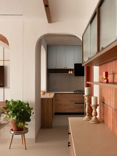 Arched kitchen nook with wooden cabinets seen past a terracotta brick counter and potted plant