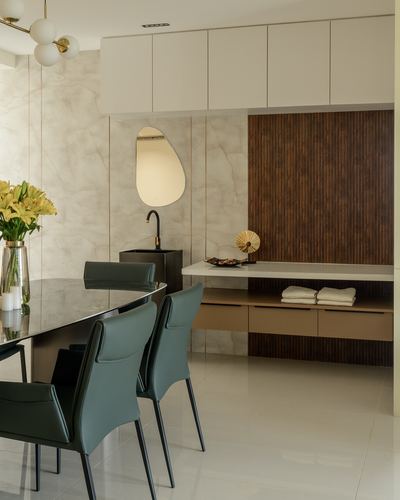 Dining table with green leather chairs beside a stone-clad wash counter and fluted wood panel wall