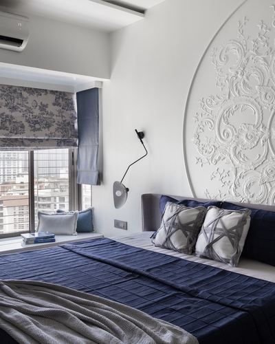 Bedroom with navy bedding, patterned blind, and large circular carved plaster wall medallion above bed