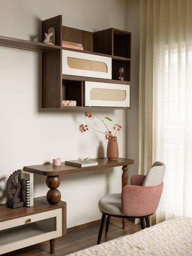 Wall-mounted wood shelving with cane drawers above a study desk and pink chair by a curtained window