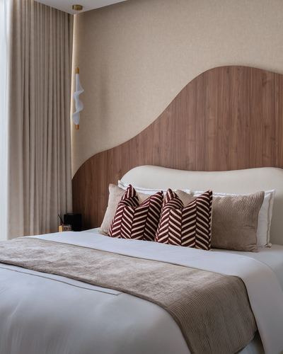 Bedroom with curved wood headboard panel, beige linens, and maroon herringbone pillows