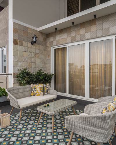 Balcony seating with wicker furniture, patterned tile floor, and stone-clad wall by sliding glass doors