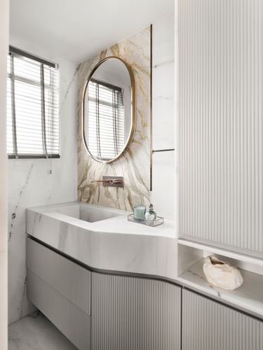 Bathroom vanity with sculptural stone sink, round brass mirror, and fluted cabinetry beside a veined stone wall.