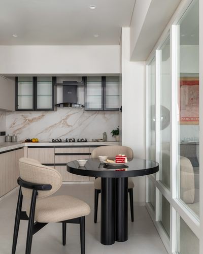 Open kitchen with marble backsplash and round black table with beige upholstered chairs by window