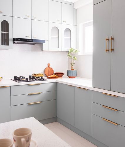 L-shaped sage-grey kitchen with white countertop, brass handles, and arched glass cabinet fronts