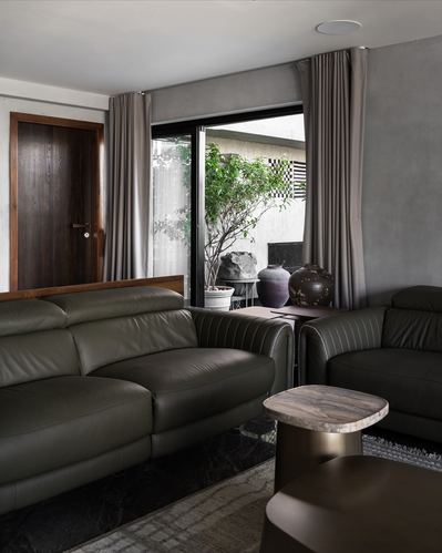 Olive leather sofas in a grey living room facing a glass door to a small garden with ceramic vases