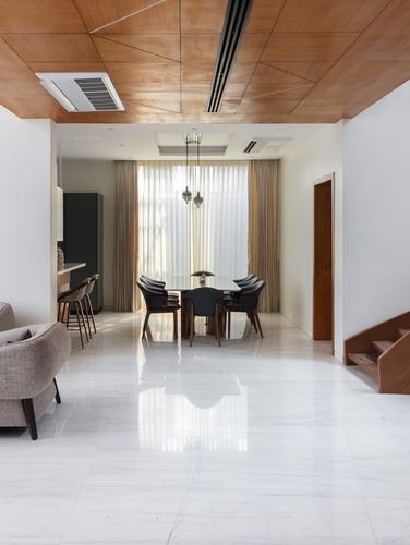 Dining area with dark chairs under wood ceiling, glossy white floor, staircase to right