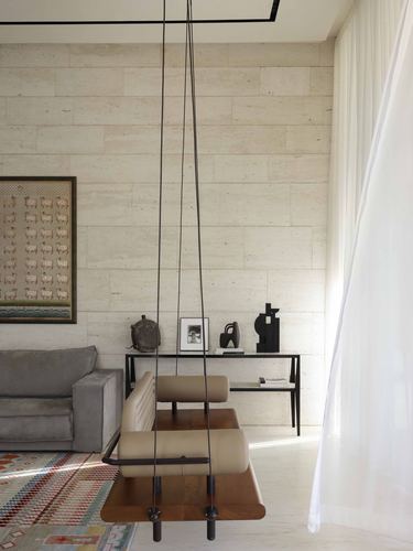 Suspended wood and leather swing bench in living room with stone-clad wall and sheer curtain
