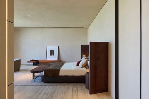Minimalist bedroom viewed through angled fluted wood partition, low bed and bench