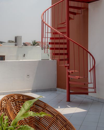 Red spiral staircase on white rooftop terrace with woven rattan chair and plant in foreground