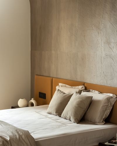 Bedroom with textured stone wall, mustard leather headboard, and layered neutral pillows.