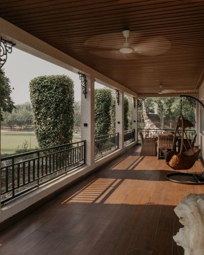 Long wooden veranda with hanging rattan swing, wicker dining set, and columns wrapped in ivy