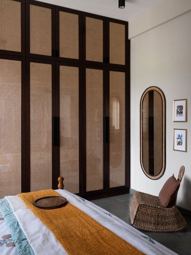 Bedroom corner with cane wardrobes, oval cane mirror, wicker chair and mustard-striped bed linen