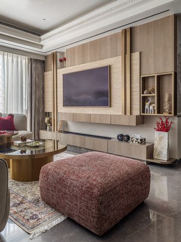 Living room with paneled wood TV wall, gold accents, maroon ottoman, and brass coffee table