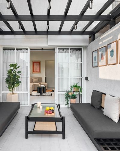 Covered balcony lounge with black pergola, charcoal sofas, glass coffee table and view into living room