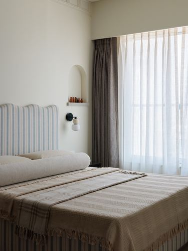Bedroom with striped headboard, arched niche shelf, and sheer curtained window in soft daylight
