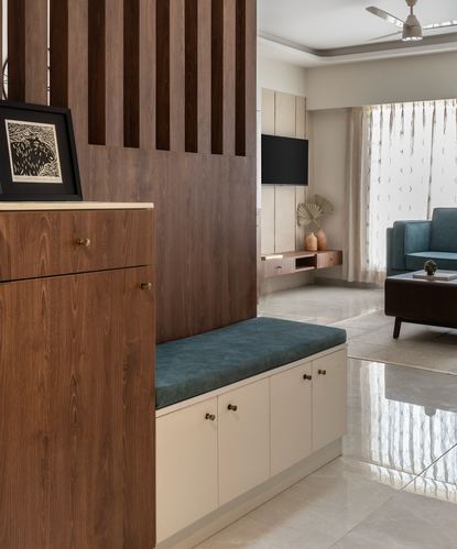 Foyer with fluted wood partition, teal-cushioned bench and cream cabinets opening to living room beyond