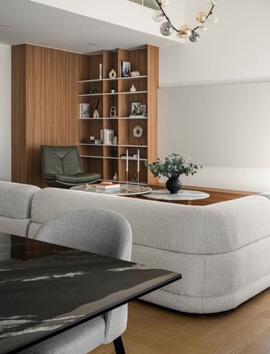 Grey boucle sofa curves in front of a wood-panelled bookshelf with a green leather chair in a contemporary living room