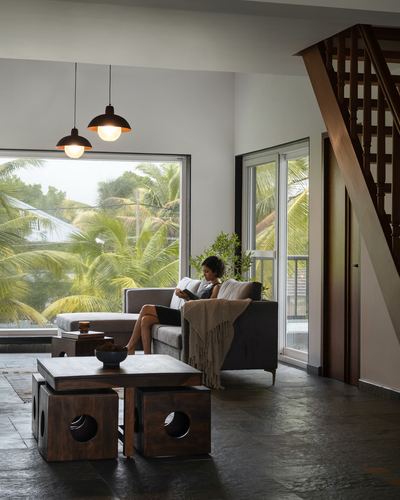 Woman reading on sofa in living room with palm view and wooden staircase