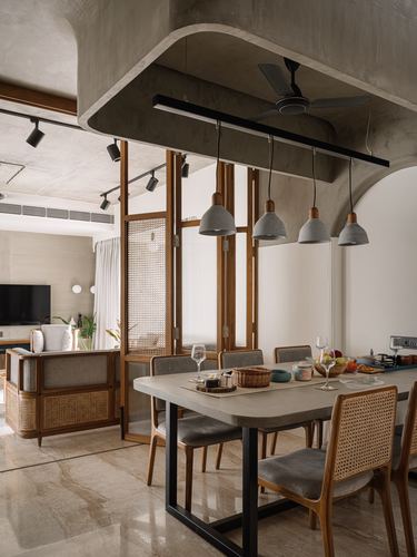 Dining table under curved concrete ceiling with four pendant lights and cane-backed chairs, cane partition doors to living room beyond