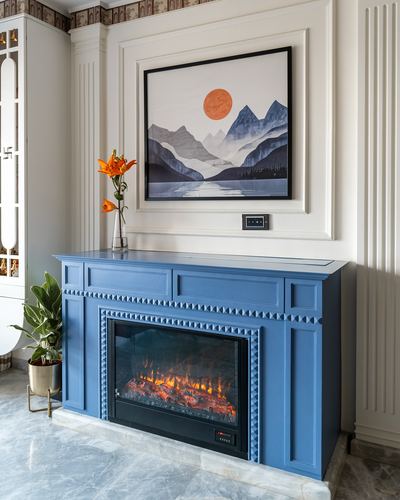 Blue carved fireplace mantel with electric insert beneath a mountain artwork on cream paneled wall