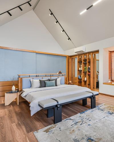 Bedroom with vaulted ceiling, wood-framed blue upholstered headboard wall, and black leather bench at foot of bed