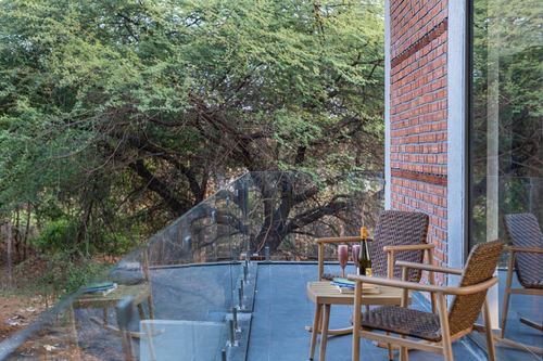 Balcony with wicker chairs and brick pier overlooking dense green trees through glass railing