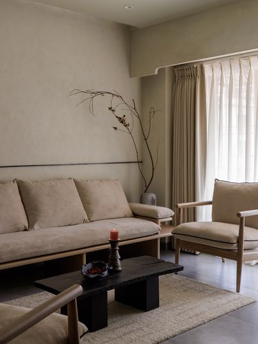 Minimalist beige living room with wood-framed sofa, armchair, dark stone coffee table and sheer curtains