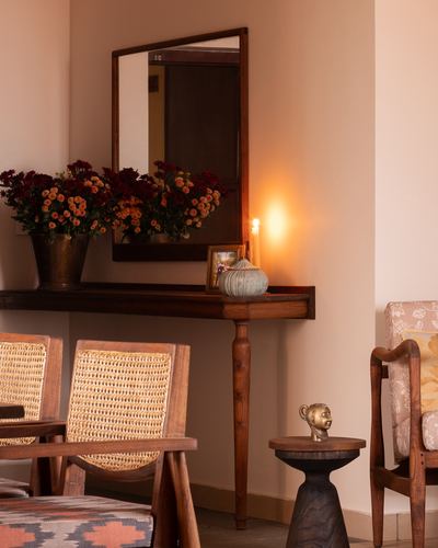 Corner vignette with wooden mirror, console table with flowers and candle, cane chairs nearby