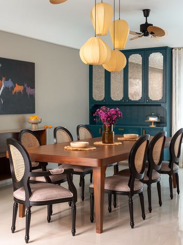 Dining room with wooden table, cane-back chairs, teal cabinet, and paper lantern pendant cluster