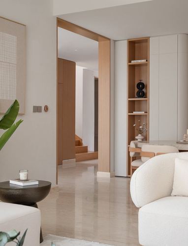 Minimalist living room with wood-framed doorway, built-in shelving, and boucle sofa on marble flooring