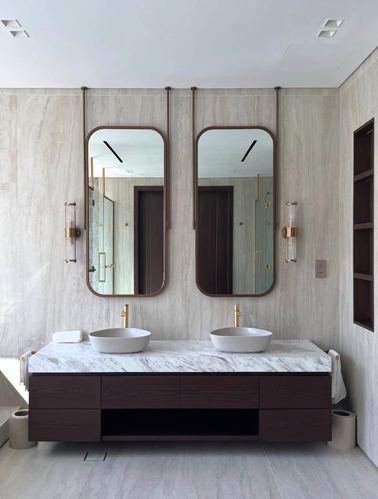 Symmetrical double vanity with vessel basins, suspended mirrors, and veined marble countertop in a stone-clad bathroom