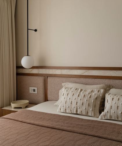 Bedroom corner with globe pendant light, stone-trimmed upholstered headboard, and textured pink and cream bedding
