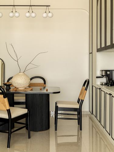 Dining nook with fluted black table, cane-back chairs, textured vase, and cabinetry beyond