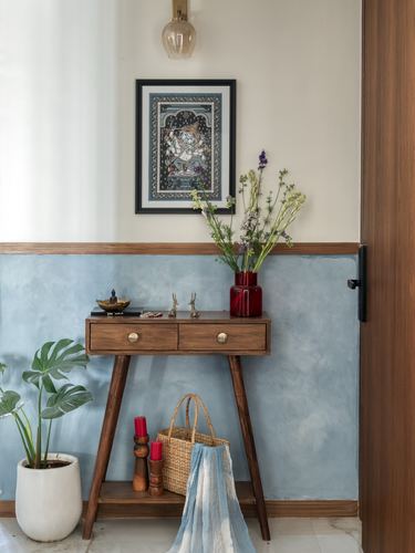 Wooden console table against a dusty blue textured wall with framed art and flowers